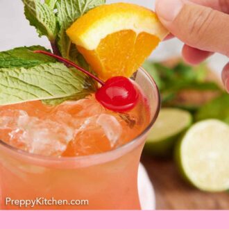 Pinterest graphic of a hand placing a small cut of orange into a glass of zombie cocktail.