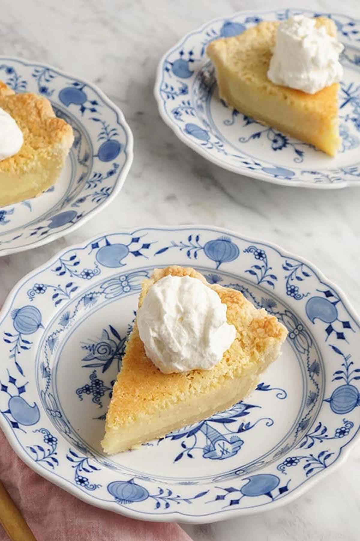 Three plates with slices of buttermilk pie with whipped cream on top.