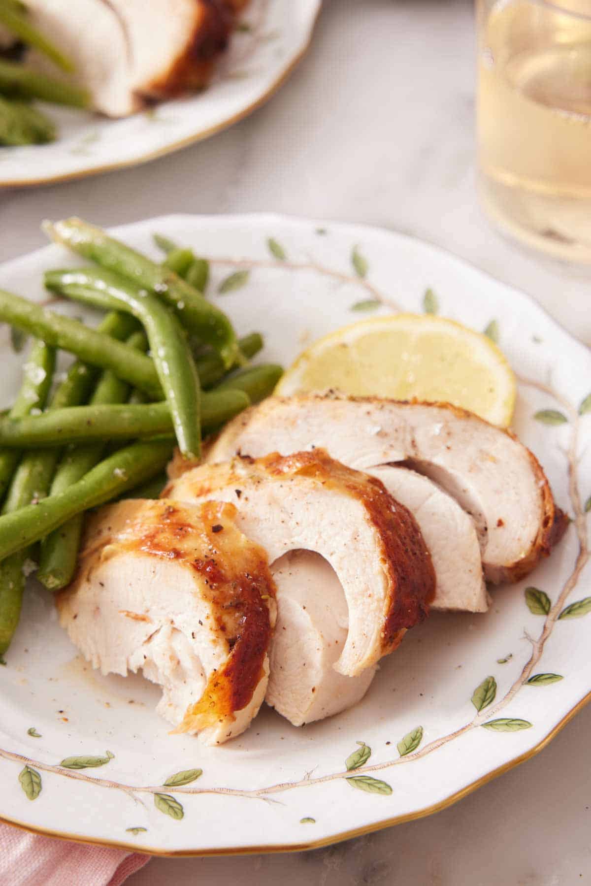 A plate with a serving of air fryer turkey breast with green beans and a lemon slice.