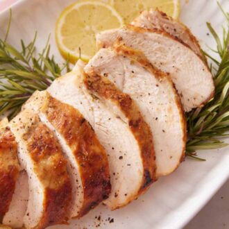A close up view of sliced air fryer turkey breast over some fresh rosemary and slices of lemon.