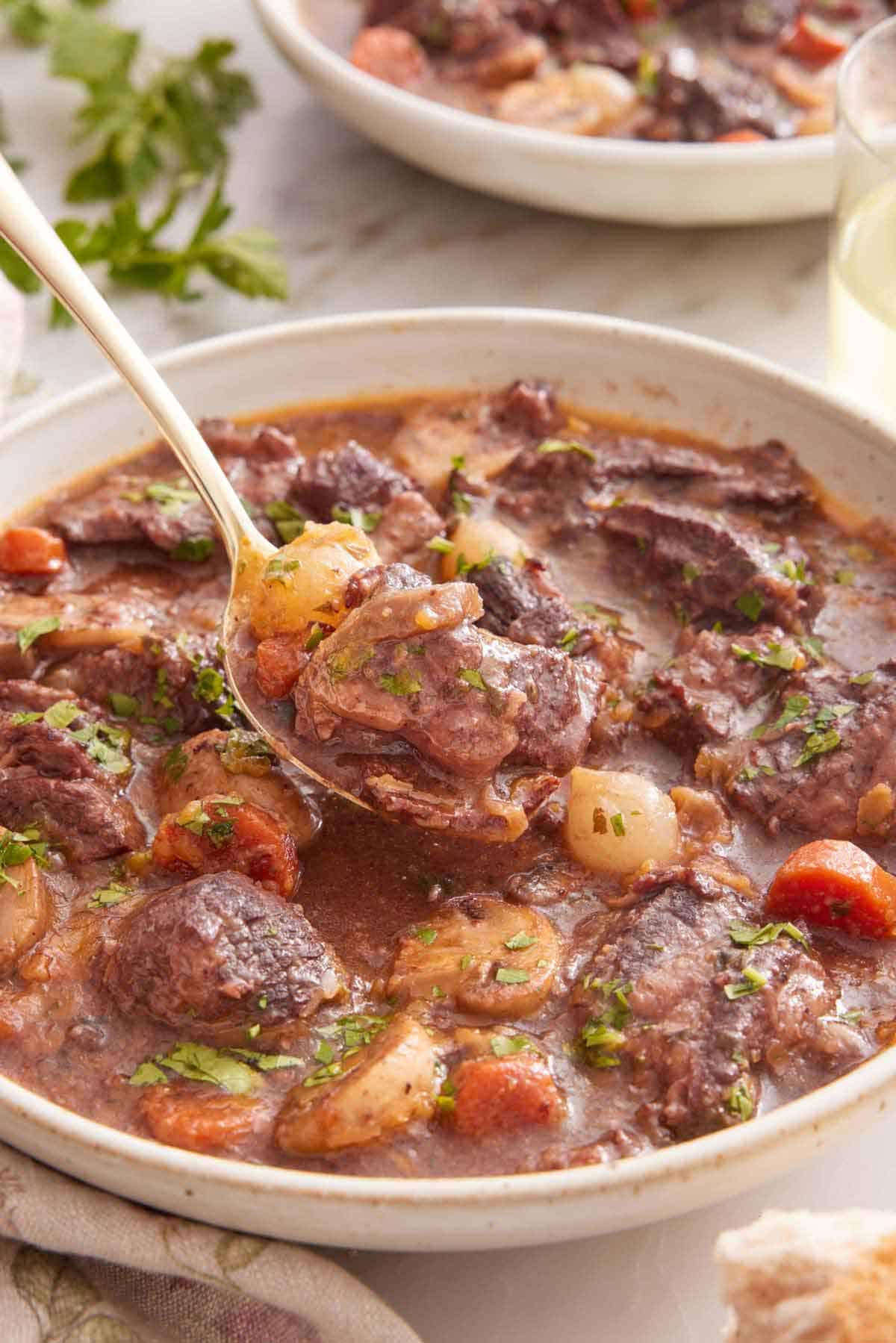 A bowl of beef bourguignon with a spoonful lifted up.