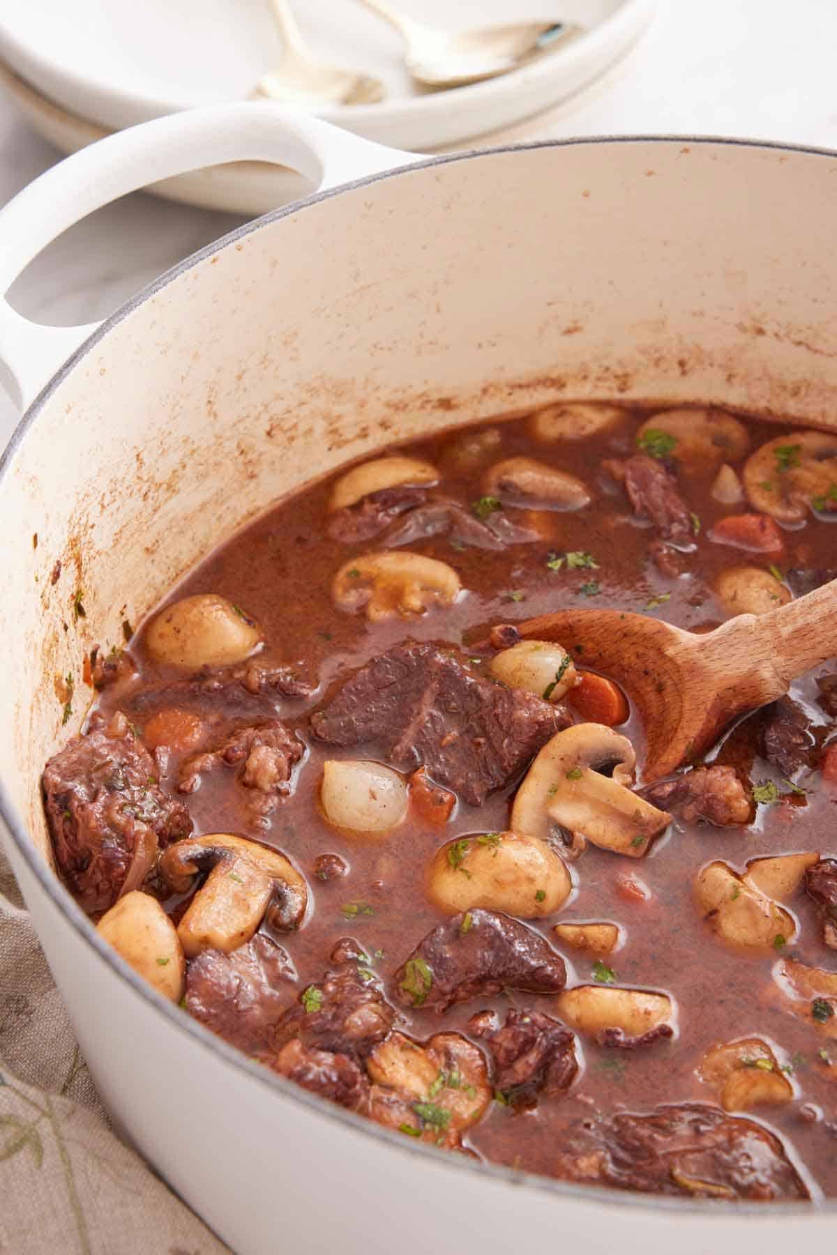 A large white pot of beef bourguignon with a wooden spoon tucked inside.