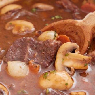 A close view of a wooden spoon inside of a pot of beef bourguignon.