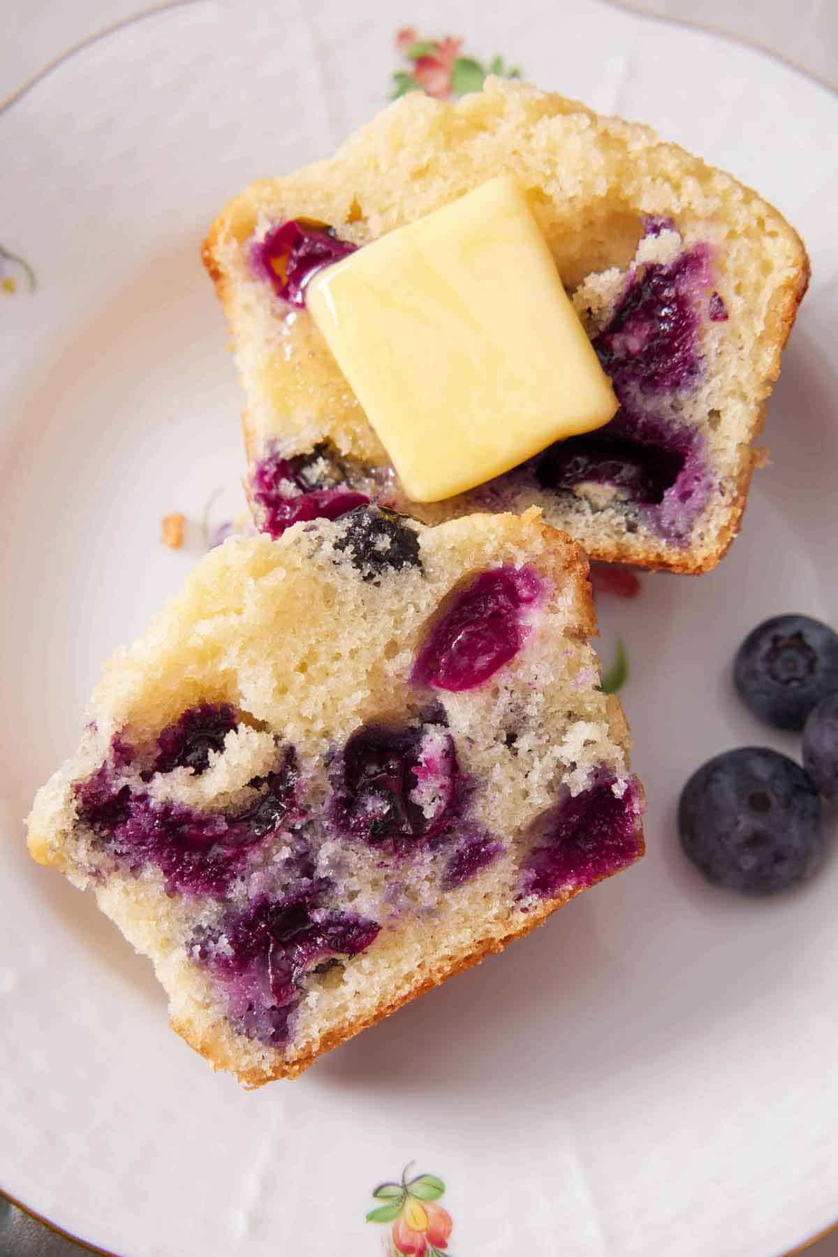 Overhead view of a blueberry muffin cut in half with a knob of butter on top.