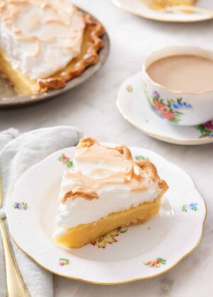 A plate with a slice of butterscotch pie with a cup of coffee in the background and the rest of the pie.