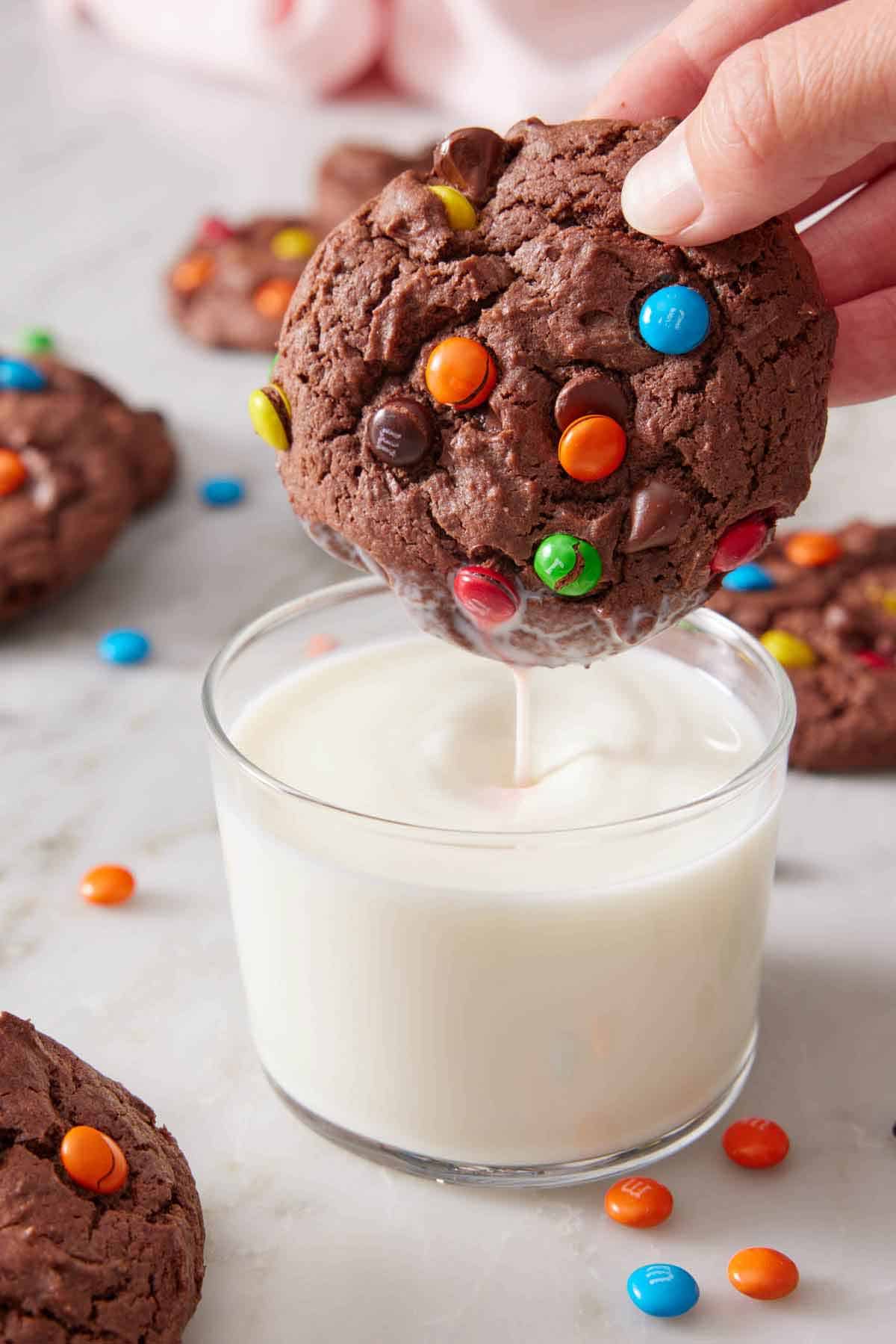 A cake mix cookie with M&M's dipped into a glass of milk and lifted.