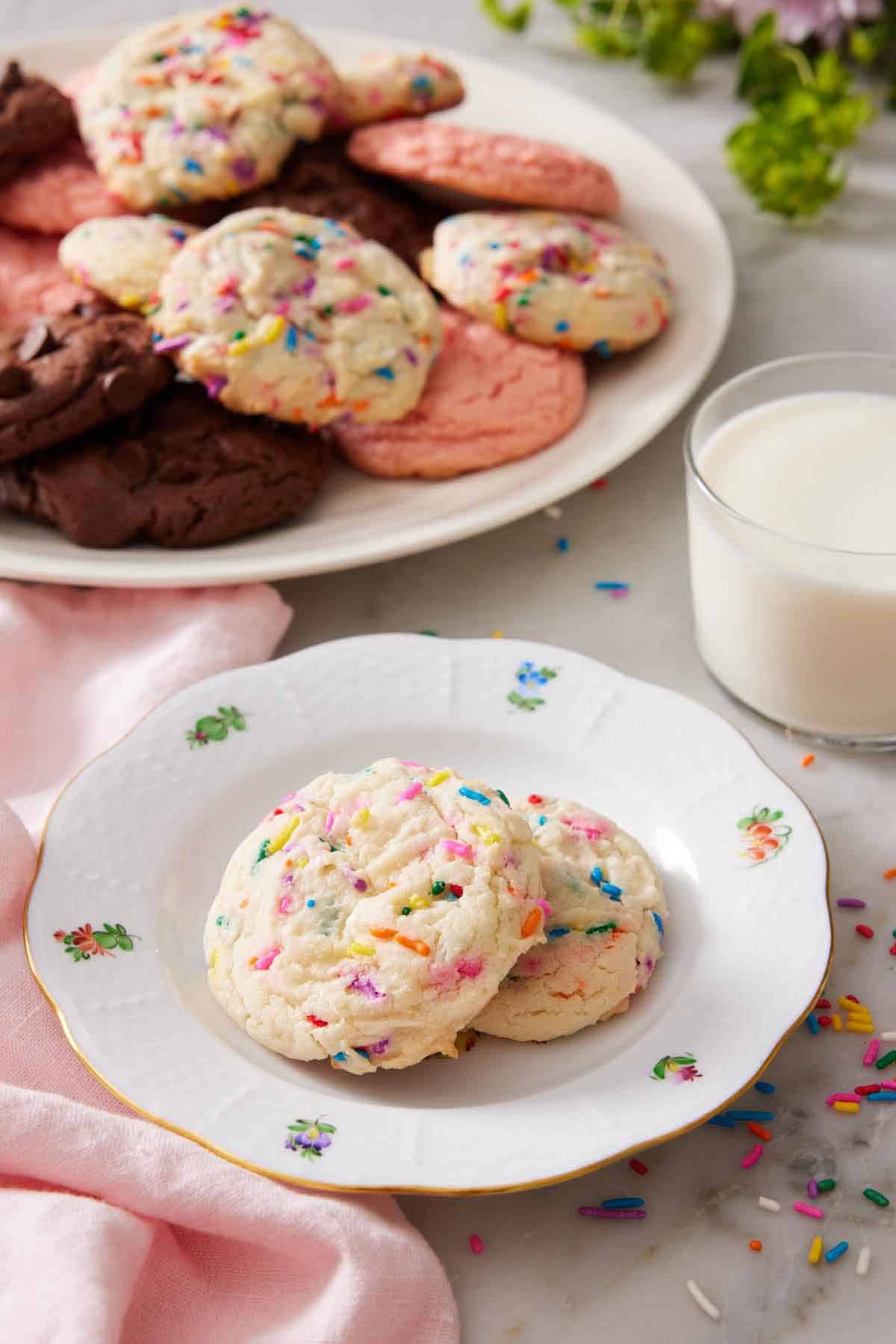 A plate with two cake mix cookies with a glass of milk and additional cookies in the background.
