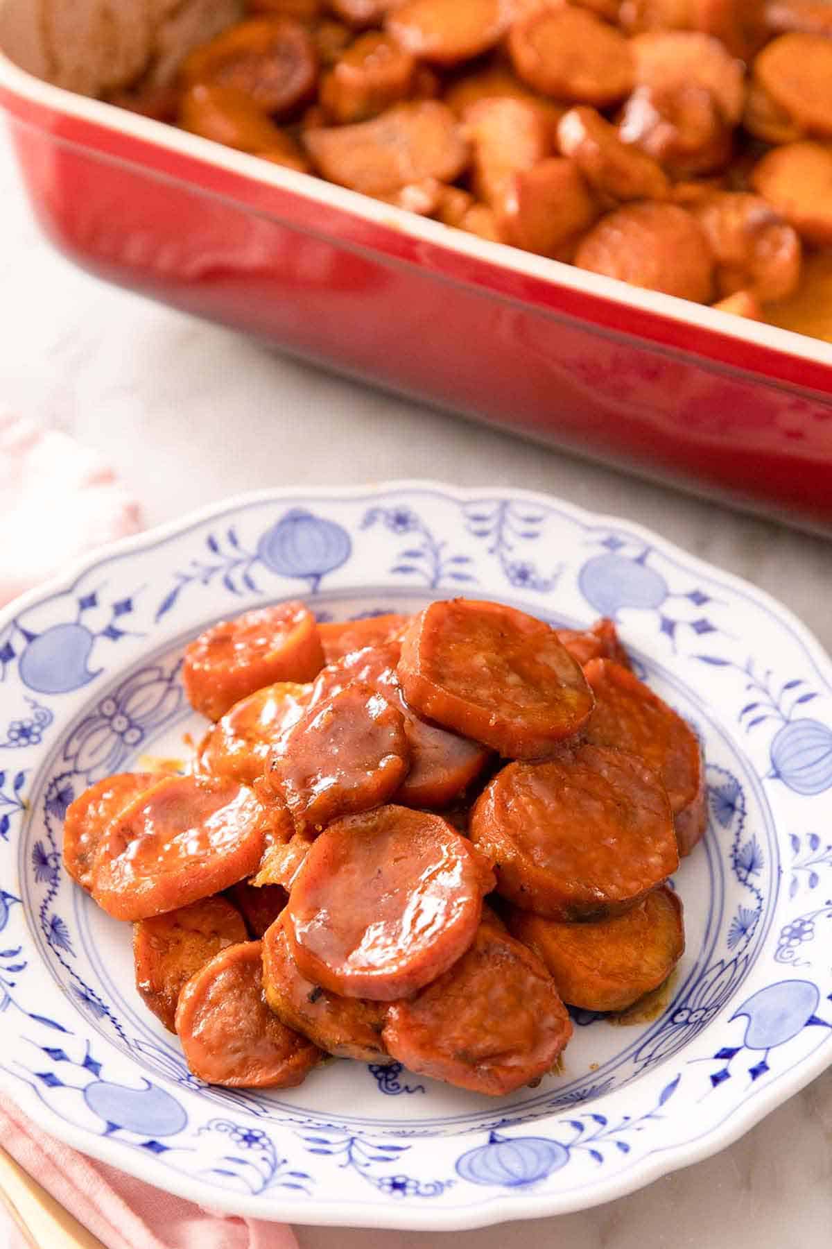 A plate with a serving of candied yams. Red baking dish with the rest in the background.
