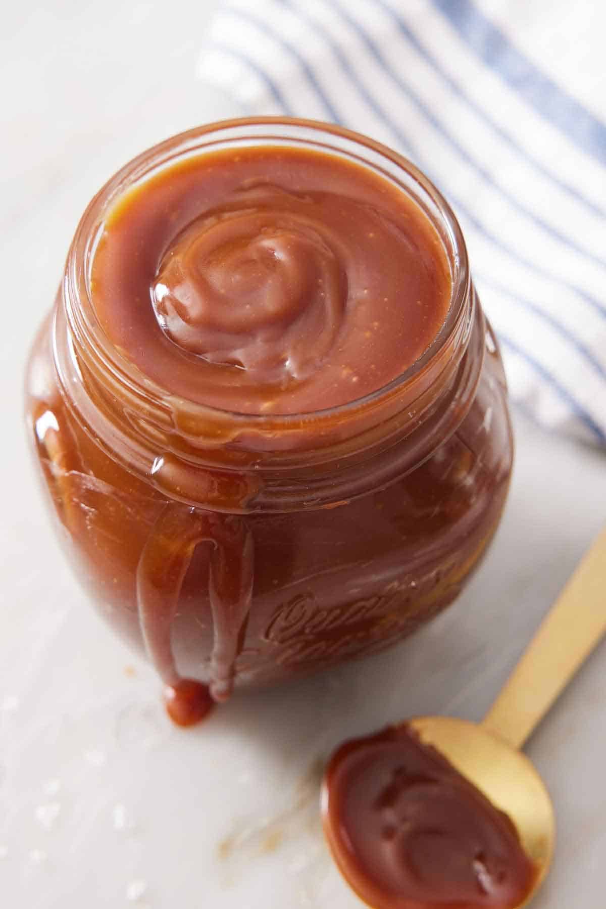 A slightly overhead view of a jar of caramel sauce with a spoon on the side.