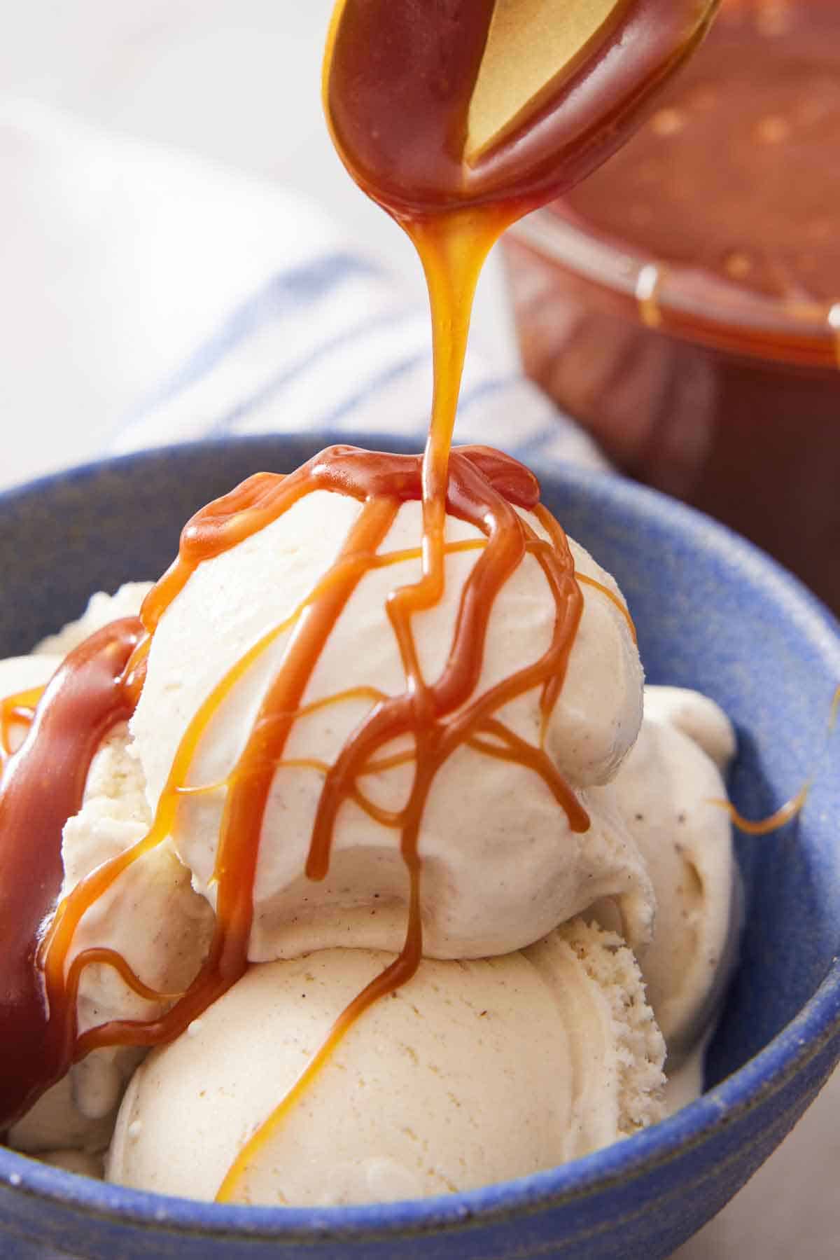 A bowl with scoops of vanilla ice cream with caramel sauce drizzled over top.