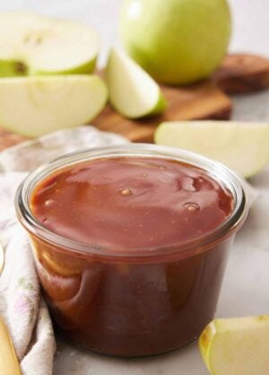 A jar of caramel sauce with some chopped apples in the background.