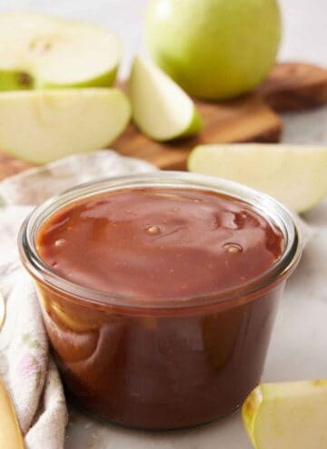 A jar of caramel sauce with some chopped apples in the background.