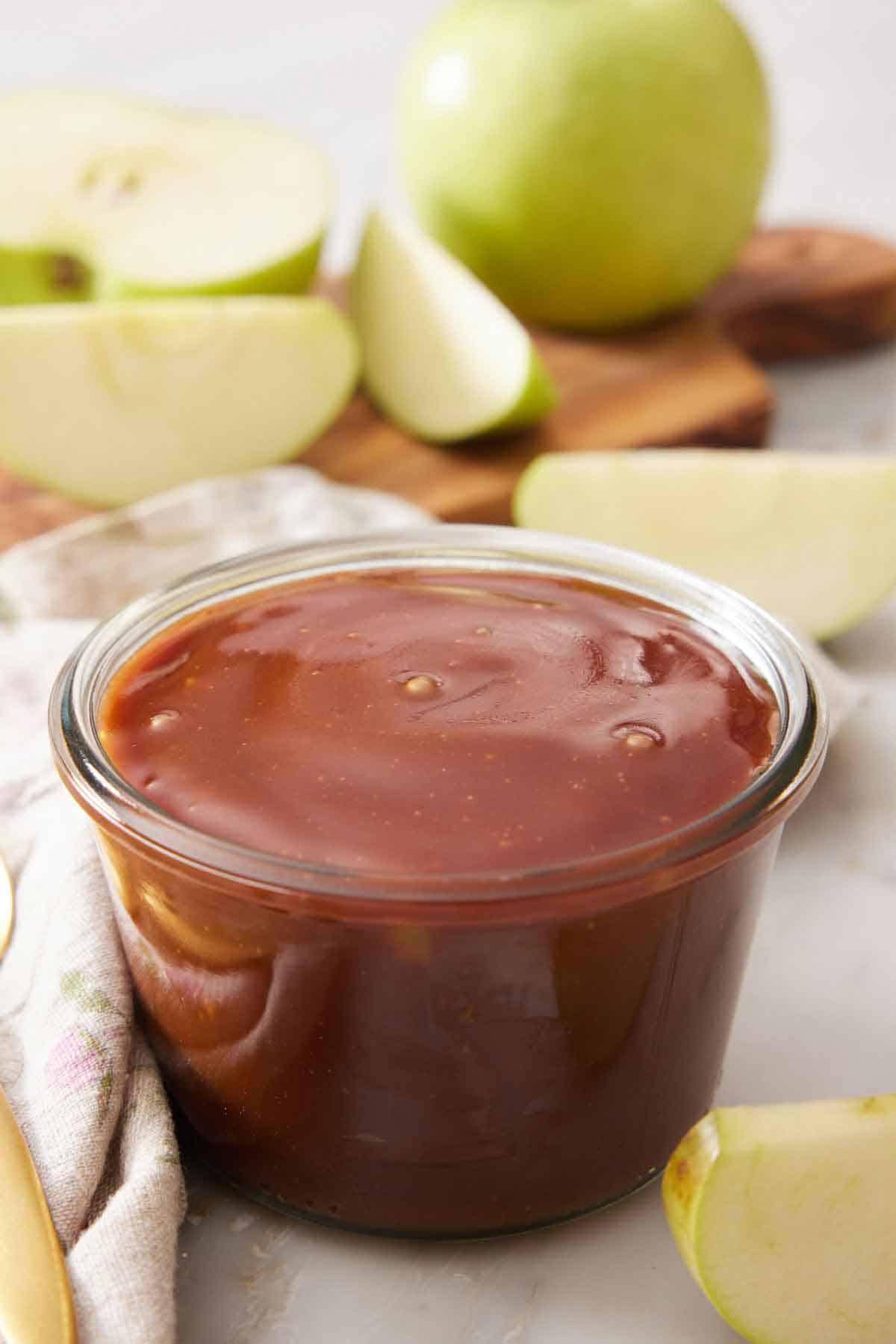 A jar of caramel sauce with some chopped apples in the background.