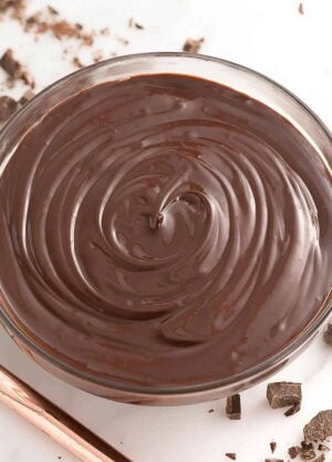 Overhead view of a bowl of chocolate ganache with chopped chocolate off to the side.