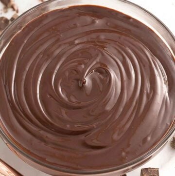 Overhead view of a bowl of chocolate ganache with chopped chocolate off to the side.
