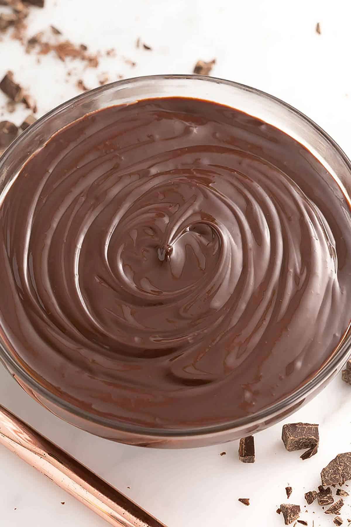 Overhead view of a bowl of chocolate ganache with chopped chocolate off to the side.