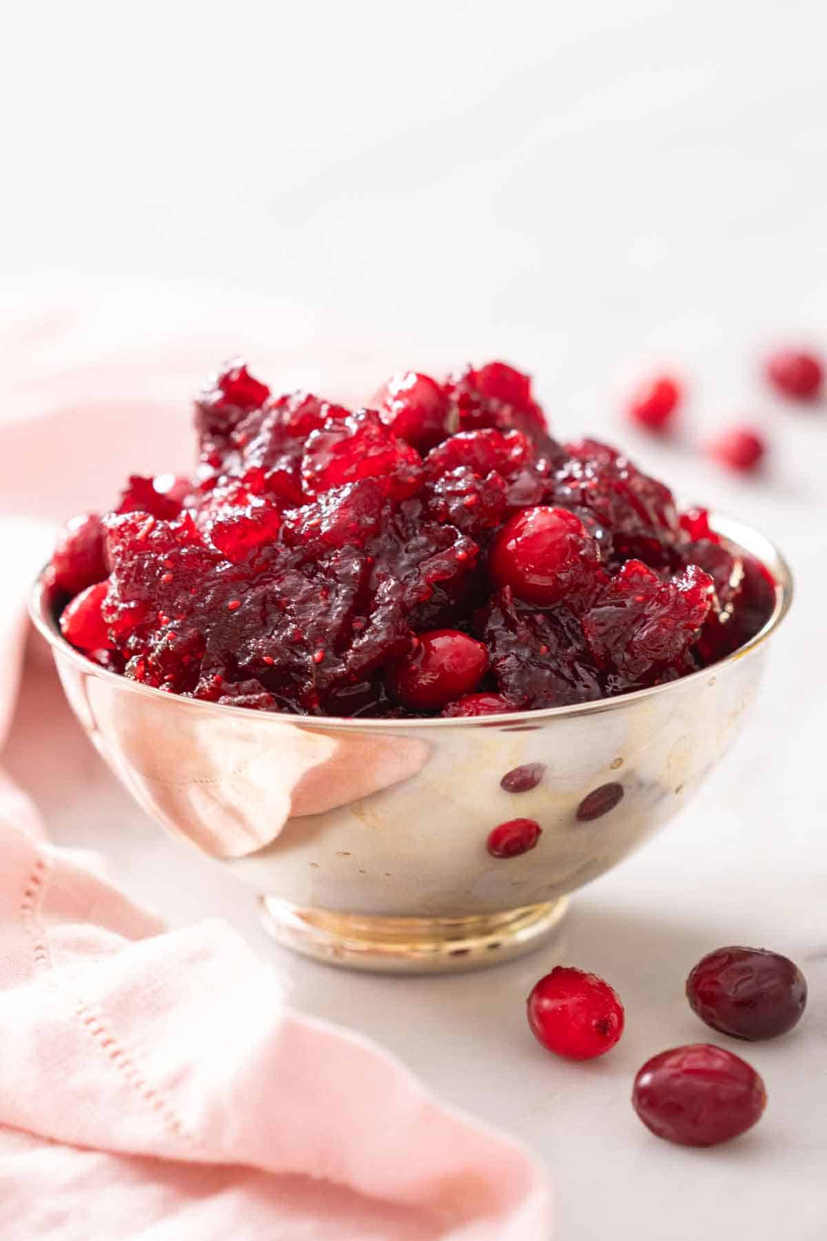 A profile view of a bowl of cranberry sauce with some cranberries scattered around.