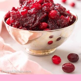 Pinterest graphic of a profile view of a bowl of cranberry sauce with some cranberries scattered around.