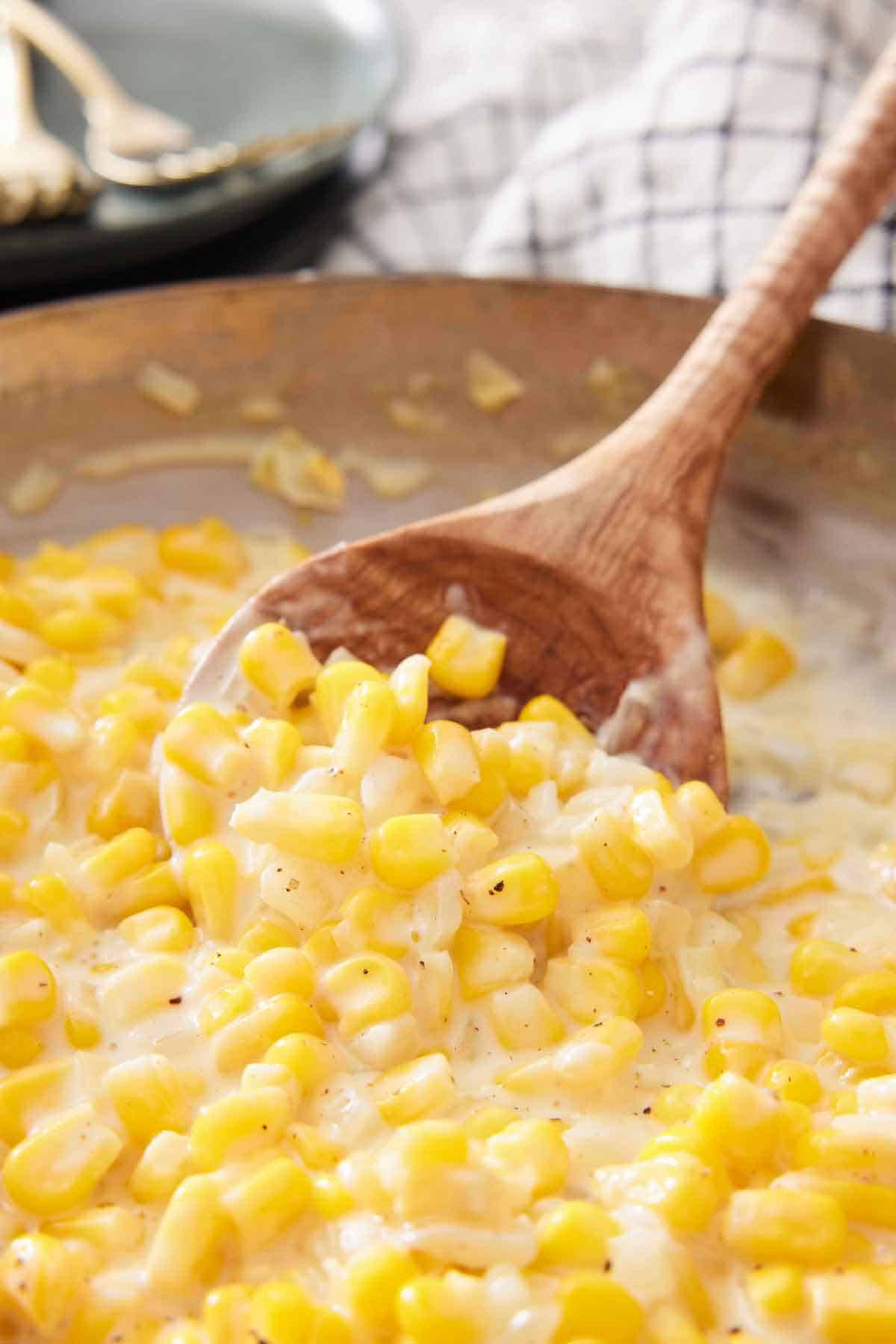 A wooden spoon scooping creamed corn in a skillet.