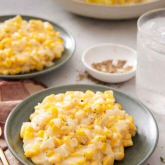 Pinterest graphic of two plates of creamed corn with a platter with more in the background along with a glass of water and bowl of pepper.