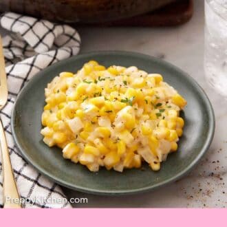 Pinterest graphic of a plate of creamed corn with a skillet with more creamed corn and a wooden spoon in the background.
