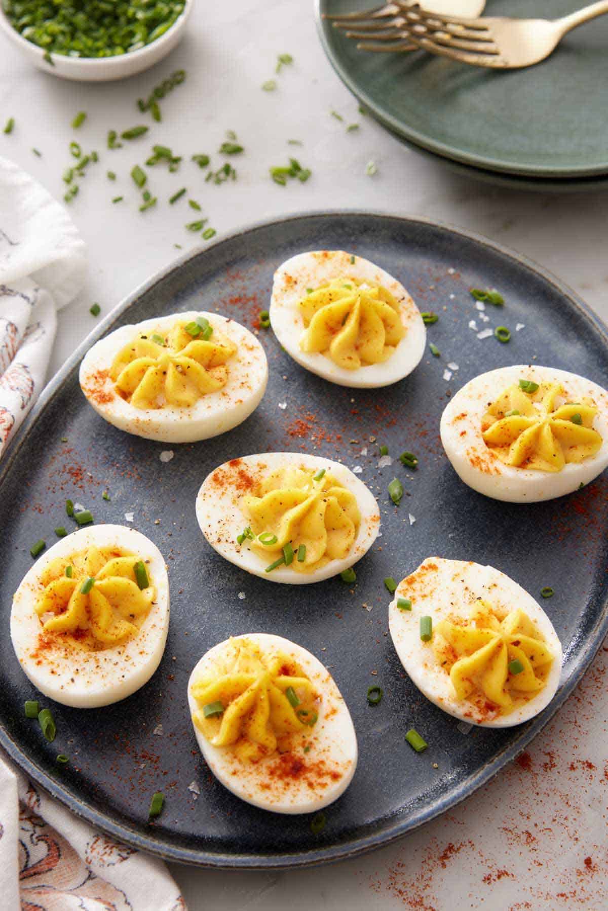 A platter with deviled eggs topped with chives and paprika.
