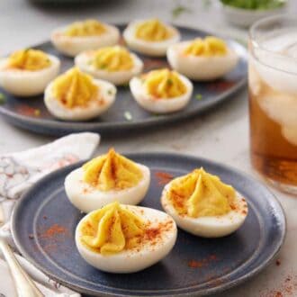 Pinterest graphic of a plate with three deviled eggs with an additional platter in the background with more. Paprika sprinkled around.