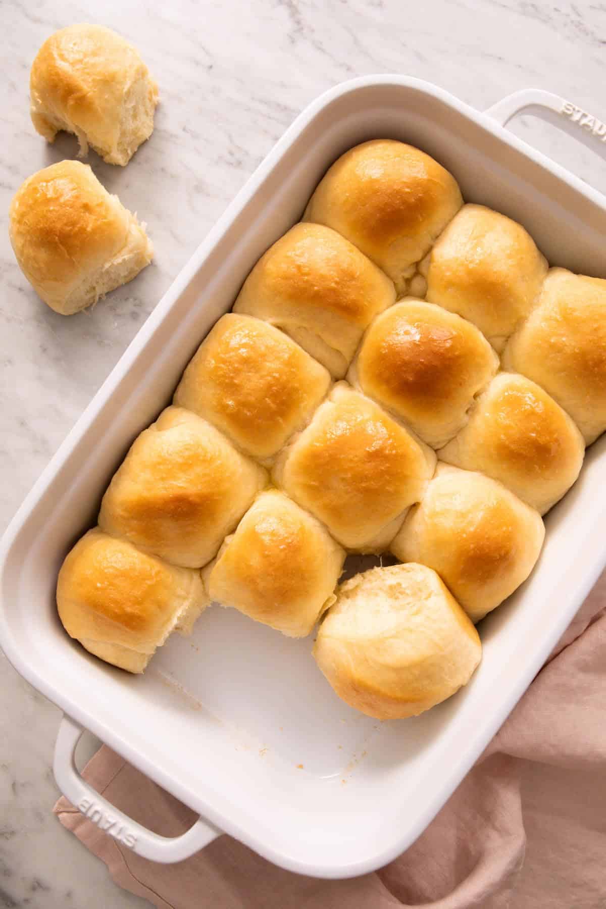 An overhead view of a baking dish with dinner rolls with two removed and placed on the side.