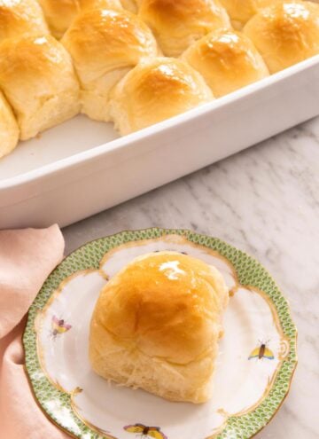 A plate with a dinner roll with a baking dish with more in the back.