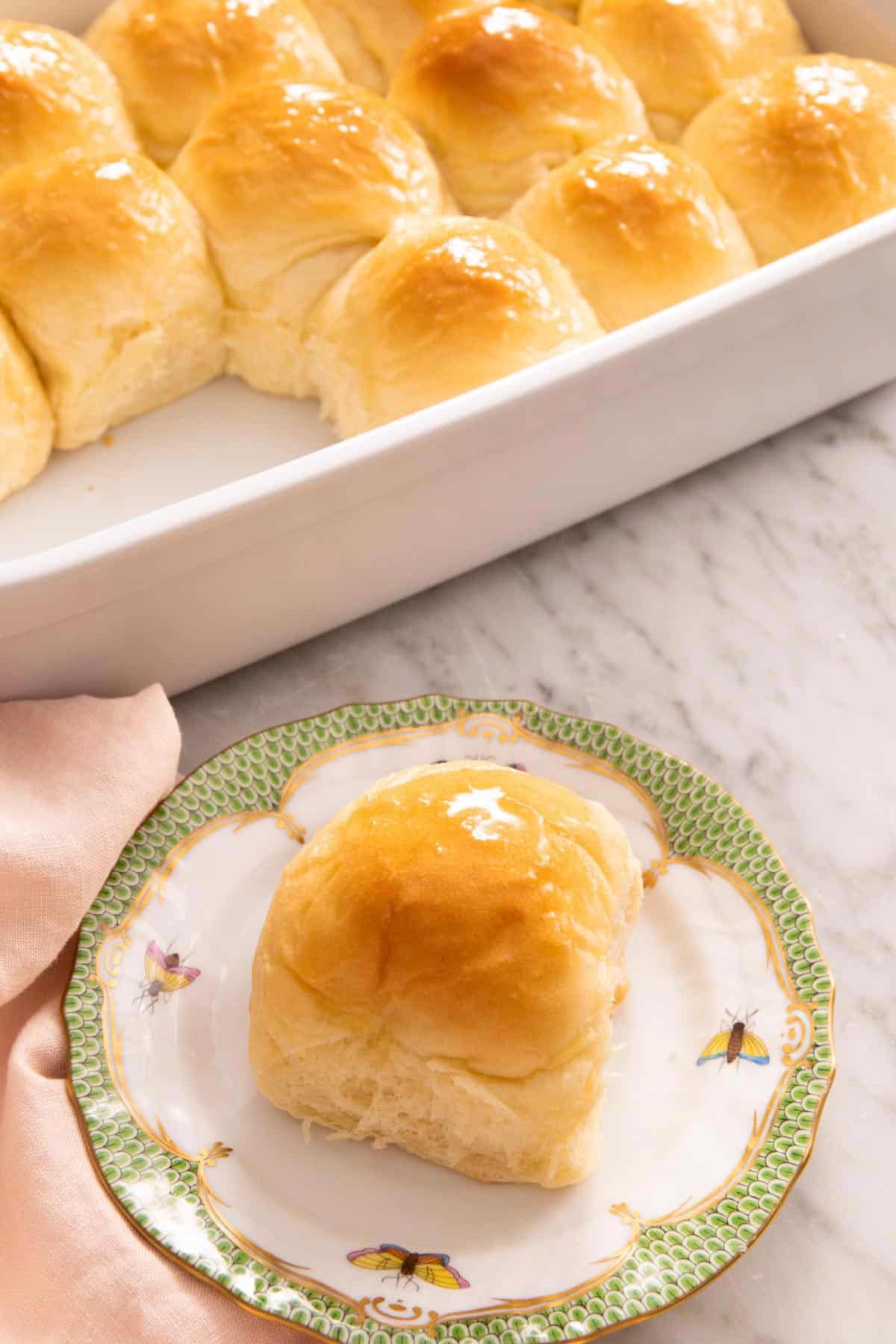 A plate with a dinner roll with a baking dish with more in the back.