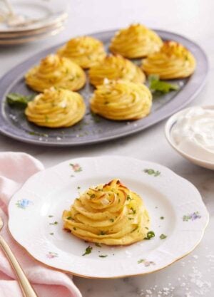 A plate with a serving of duchess potatoes with a platter with more in the background.
