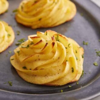 A close up view of duchess potatoes on a platter with the focus on one. All garnished with chopped parsley.