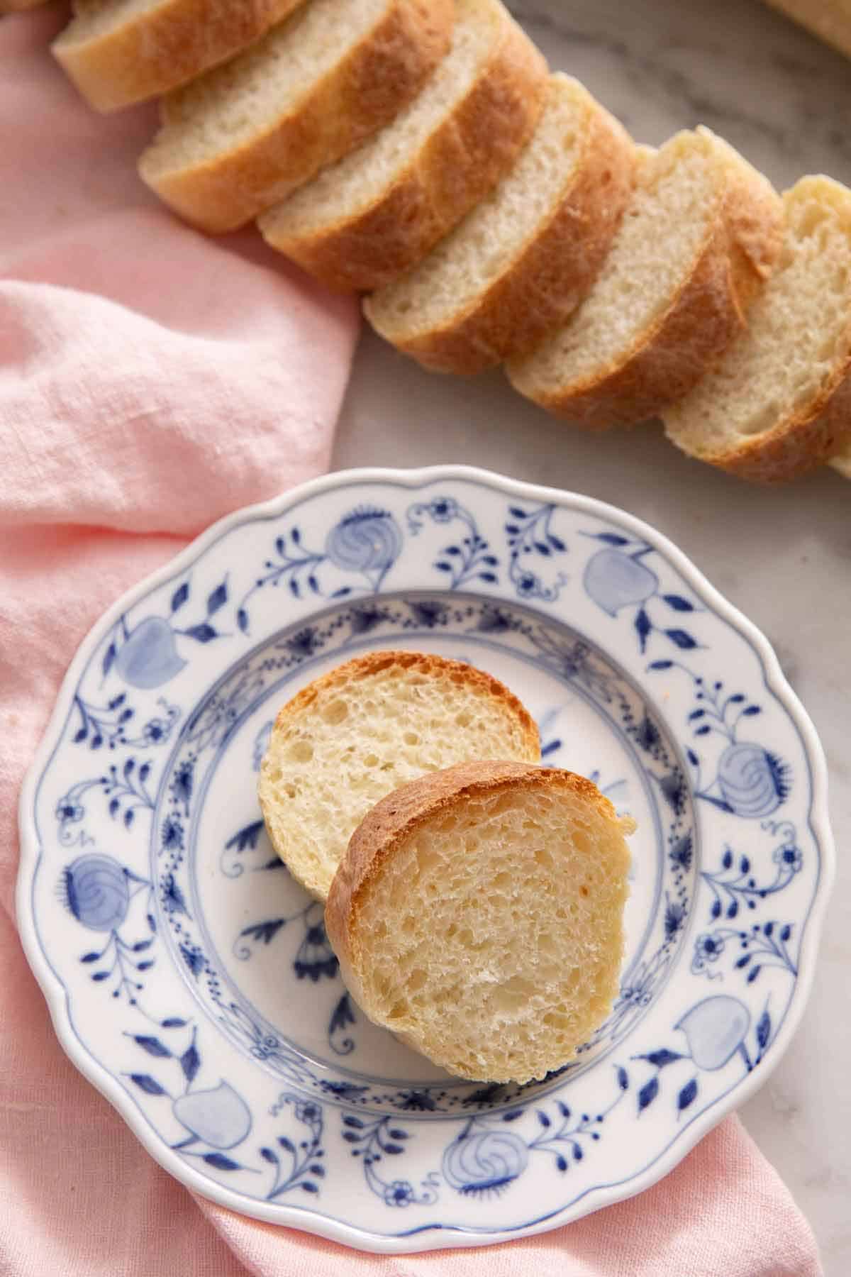 A plate with two slices of French bread with a sliced loaf in the background.