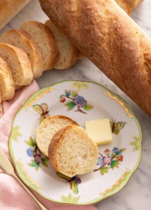 A plate with two slices of French bread with a knob of butter surrounded by more loaves of French bread.
