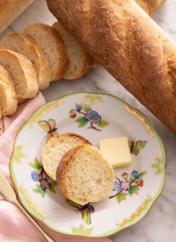A plate with two slices of French bread with a knob of butter surrounded by more loaves of French bread.