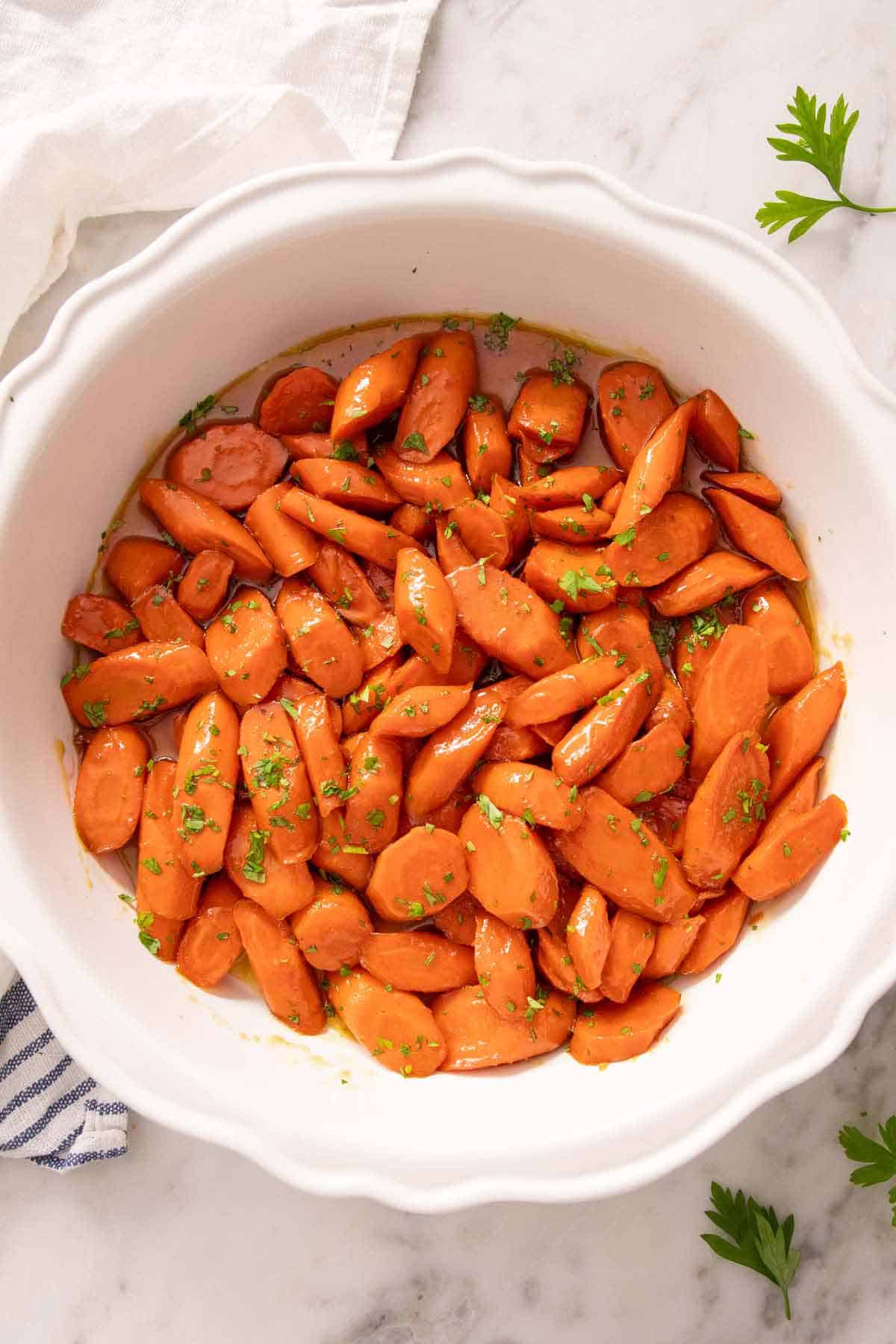 Overhead view of a bowl of glazed carrots topped with chopped parsley.