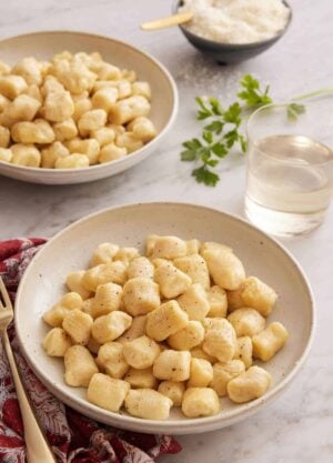 Two plates of gnocchi with a glass of wine and bowl of cheese.