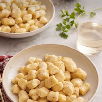 Pinterest graphic of two plates of gnocchi with a glass of wine and bowl of cheese.
