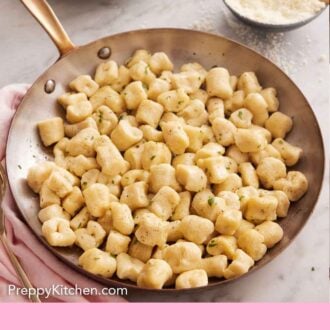 Pinterest graphic of a skillet of gnocchi with a a bowl of cheese and stack of plates in the background.
