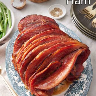 Pinterest graphic of a platter with a honey baked ham with a stack of plates, bowl of bread, and some green beans off to the side.