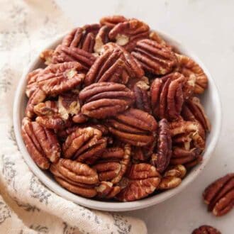 A bowl of toasted pecans with a linen beside it.