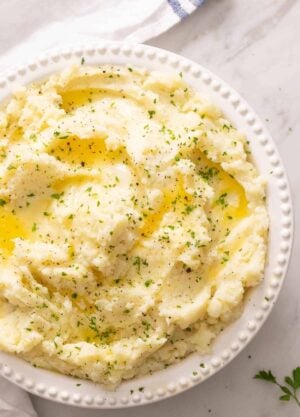 Overhead view of a bowl of mashed potatoes topped with melted butter and herbs.