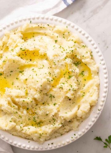 Overhead view of a bowl of mashed potatoes topped with melted butter and herbs.