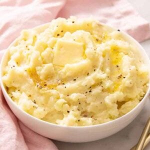 A bowl of mashed potatoes with pepper, melted butter, and a pat of butter on top.