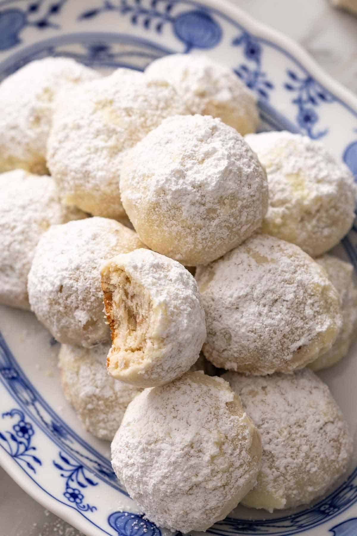 A platter of Mexican wedding cookies, one on top with a bite taken out.