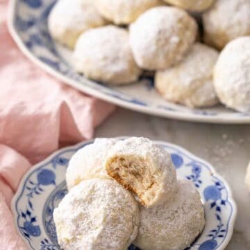 A plate with multiple Mexican wedding cookies, one on top with a bite taken out.