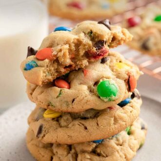 Pinterest graphic of a stack of three and a half monster cookies on a plate. Glass of milk in the background and more cookies.