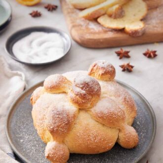 Pinterest graphic of a loaf of Pan de Muerto with a wooden serving board in the back with sliced bread.