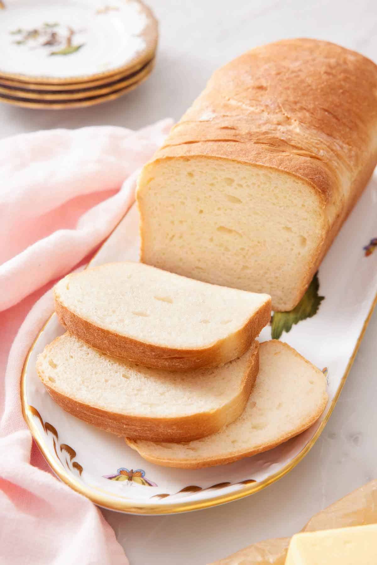 A platter with a loaf of potato bread with three slices cut in front of it.