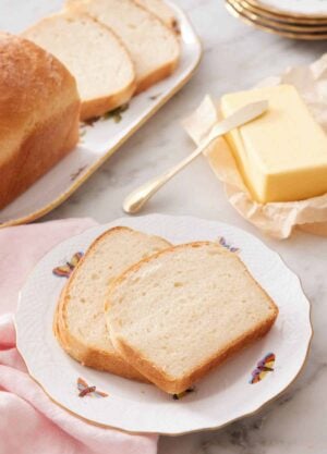 A plate with two slices of potato bread with butter and the rest of the bread in the background.